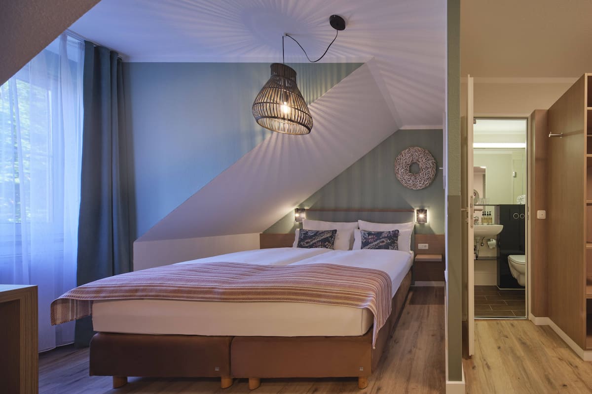 A bedroom with a large bed, a ceiling lamp, and a view into the bathroom.