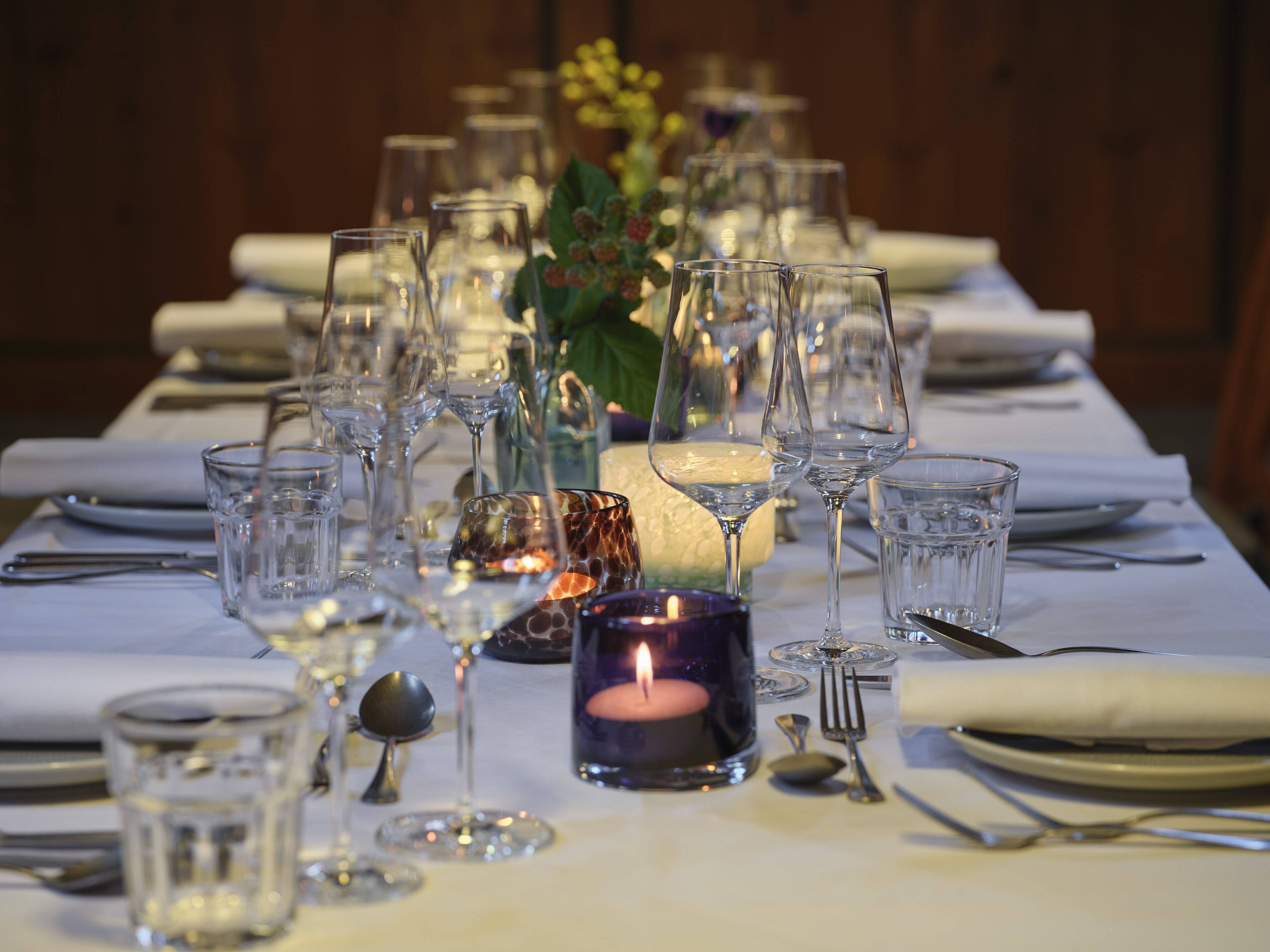 A table set for a meal with multiple wine glasses, a candle, and a vase with flowers.