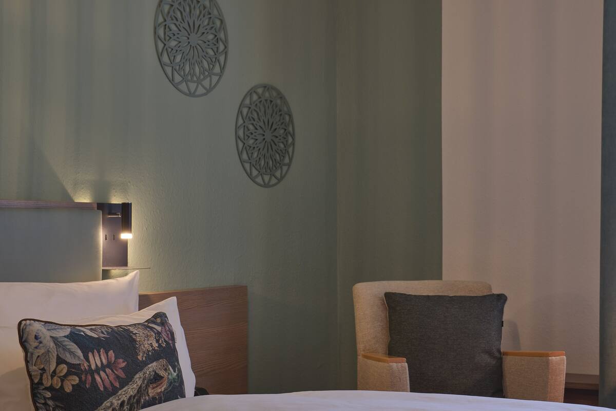 A hotel room with a bed, a chair, and two wall decorations.