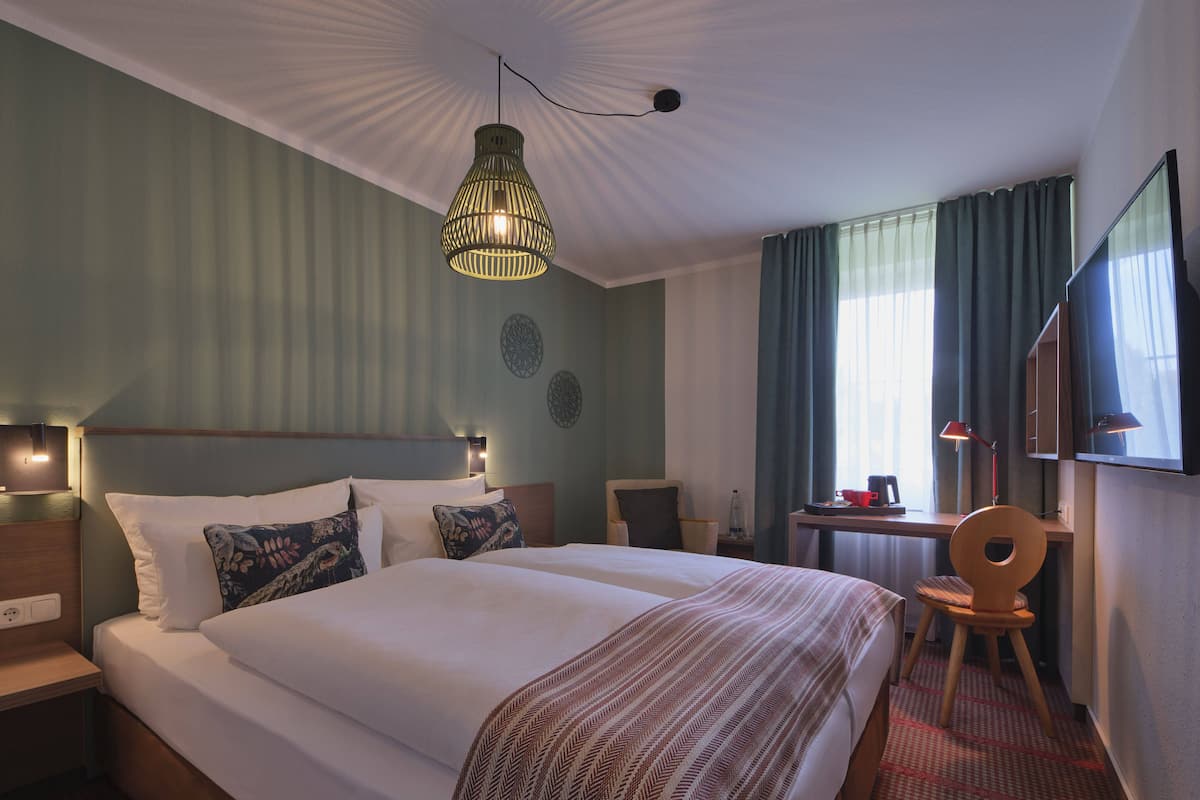 A hotel room with a large bed, a desk with a chair, a television, and a hanging light fixture.