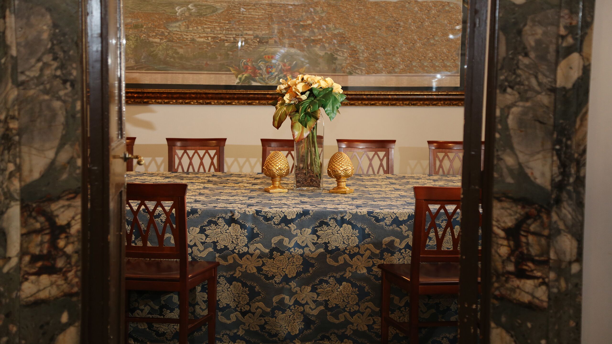 Una mesa de comedor con mantel floreado, rodeada de sillas de madera con diseños elaborados en el respaldo.