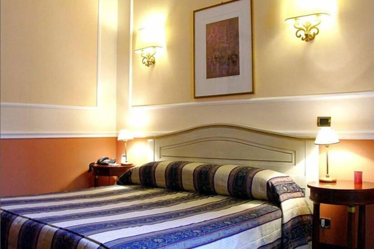 A hotel room with a bed, two bedside tables, a nightstand, and wall-mounted lamps.