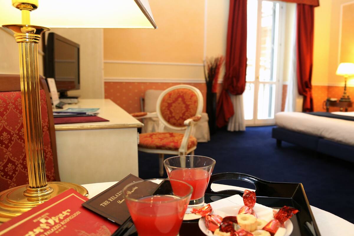 A hotel room with a desk, a chair, a bed, and a dining table with a tray of snacks and drinks.