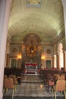 An interior with a high ceiling, ornate decorations, and a central altar. Rows of chairs are arranged facing the altar.