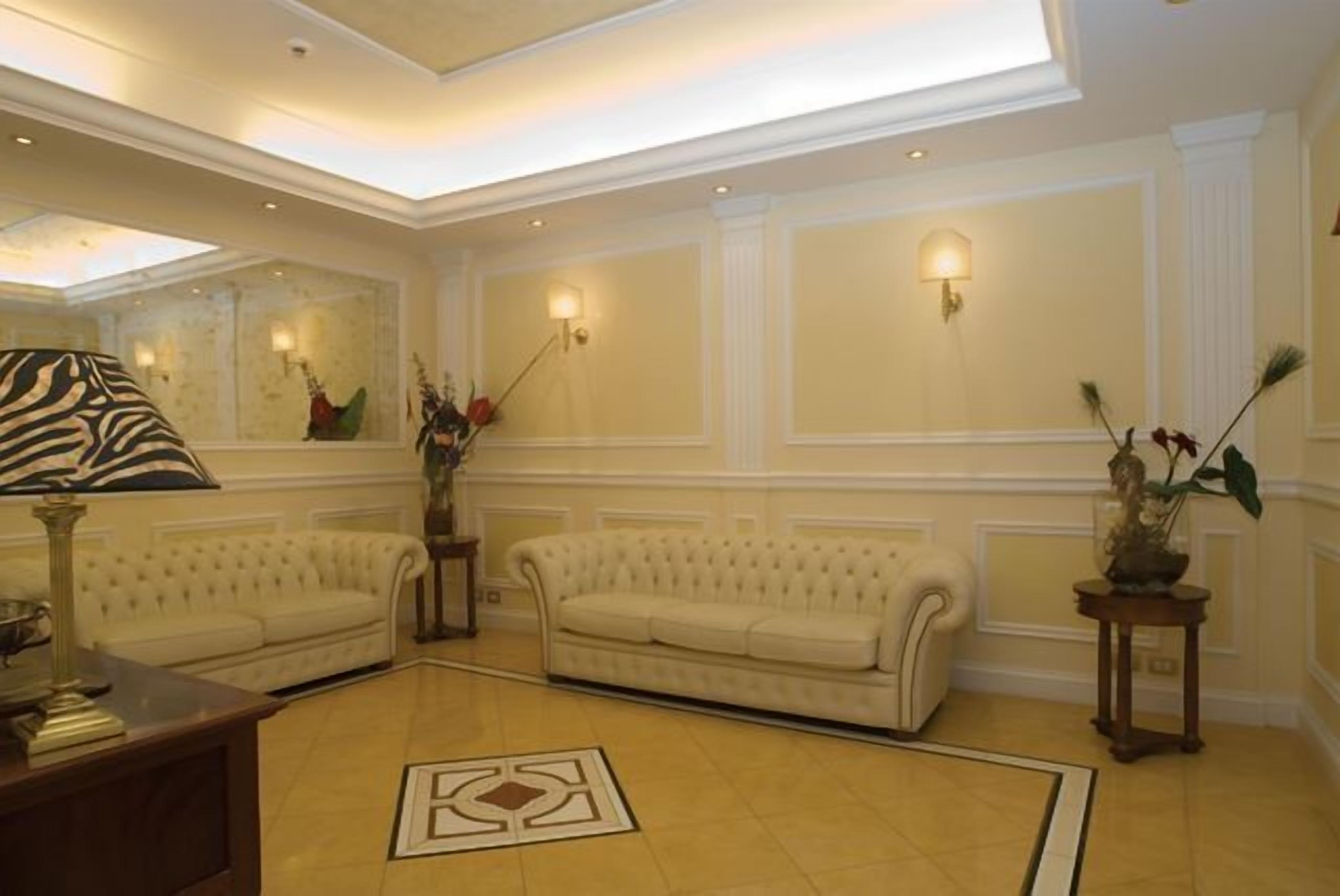 Un vestíbulo amplio con dos sofás blancos tapizados, una mesa de centro de madera y un espejo decorativo.
