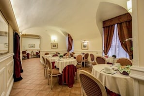 A dining area with round tables, chairs, and red curtains. - Antico Palazzo Rospigliosi (Rome)