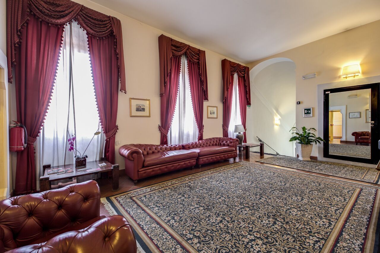 A room with a large red sofa, a matching armchair, a patterned rug, and a large mirror reflecting the room.