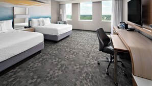 A hotel room with two beds, a desk with a chair, a flat-screen TV, and large windows offering a view of the landscape. - Courtyard by Marriott Edmonton Downtown (Edmonton)