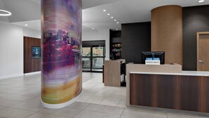 A modern hotel lobby with a reception desk, a large pillar with a cityscape mural, and a glass door entrance. - Courtyard by Marriott Edmonton Downtown (Edmonton)