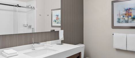 A modern bathroom with a large mirror, a white sink, a toilet, and a towel rack.