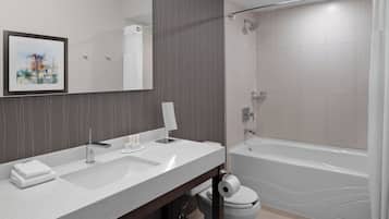 A modern bathroom with a large mirror, two sinks, a toilet, and a bathtub.