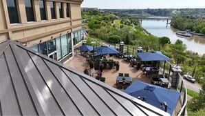 A rooftop patio with outdoor seating and a view of a river and bridge. - Courtyard by Marriott Edmonton Downtown (Edmonton)