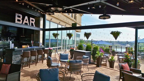 An outdoor bar area with wicker furniture, hanging plants, and a view of the landscape. - Courtyard by Marriott Edmonton Downtown (Edmonton)