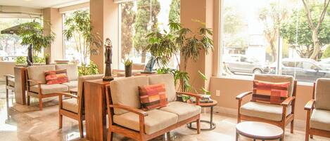 A hotel lobby with seating arrangements, large windows, and indoor plants.