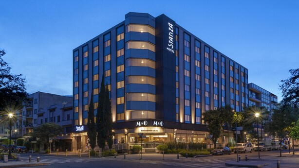 A modern hotel with a prominent 'STANZA HOTEL' sign, a 'M&OM' restaurant, and a well-lit facade. - Hotel Stanza (Mexico City)