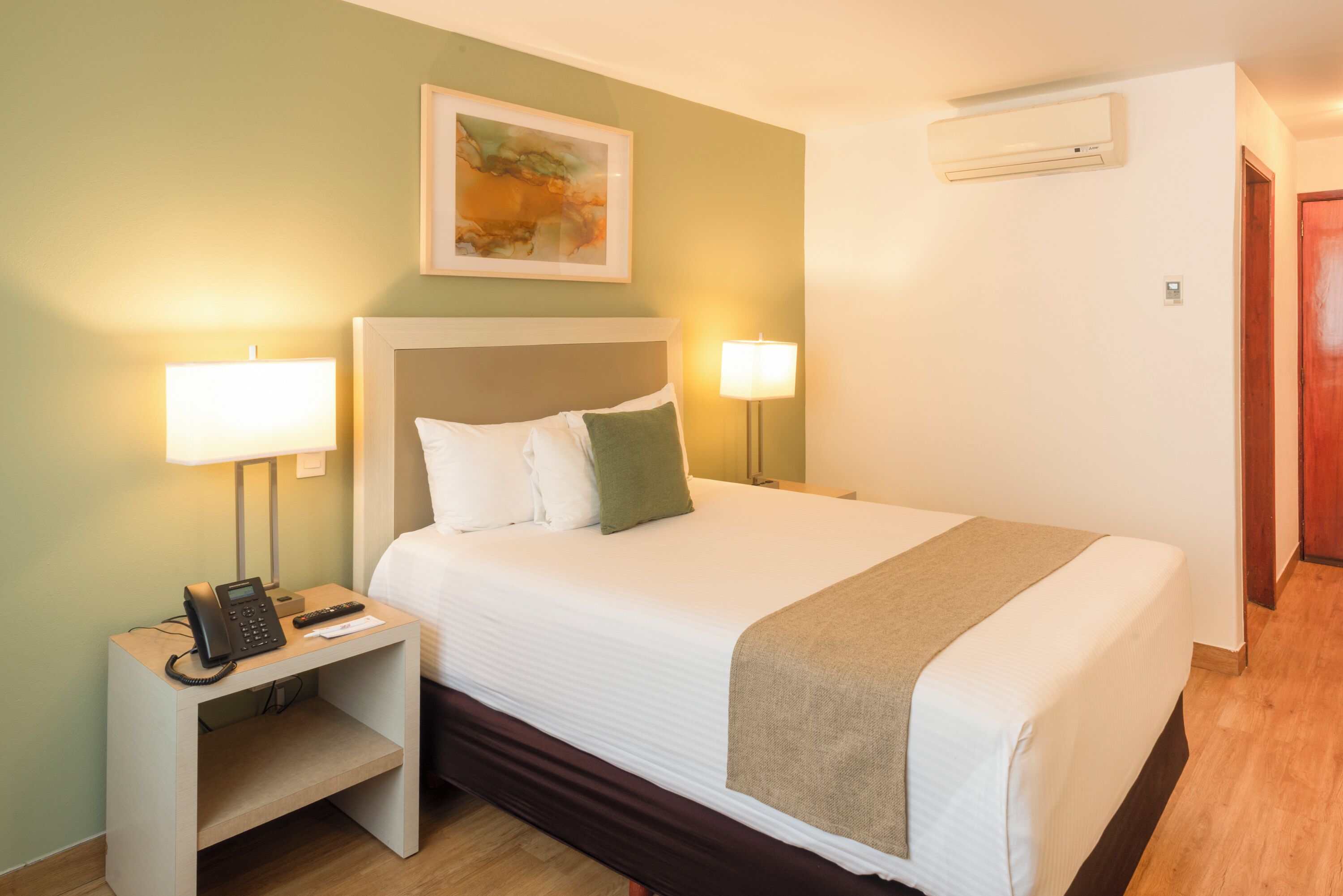A hotel room with a bed, bedside lamps, a telephone, and a painting on the wall.