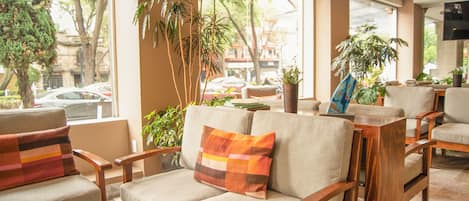 A seating area with cushioned chairs and a sofa, wooden furniture, and potted plants.