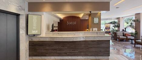 A hotel reception area with a modern design, featuring a reception desk, seating area, and a large window providing a view of the outdoors.