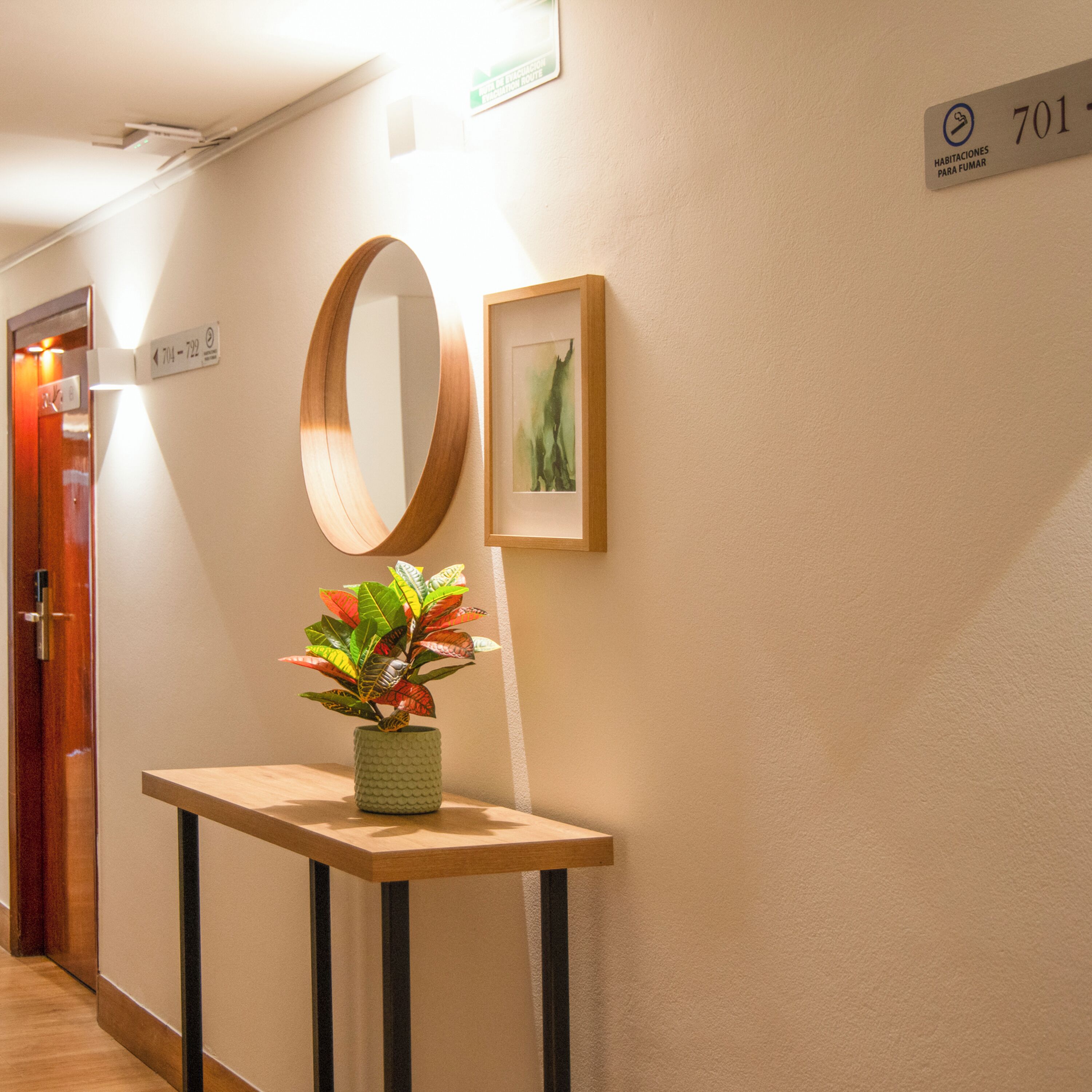 Un pasillo con una consola de madera, un espejo, una obra de arte enmarcada y un cartel que indica la habitación 701.