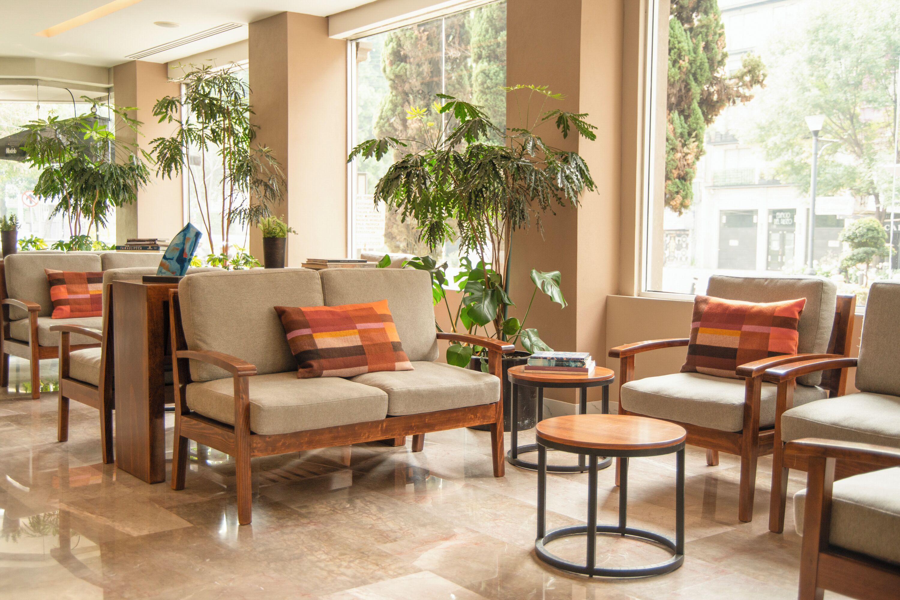 A modern lobby with sofas, armchairs, and a coffee table, featuring large windows and indoor plants.
