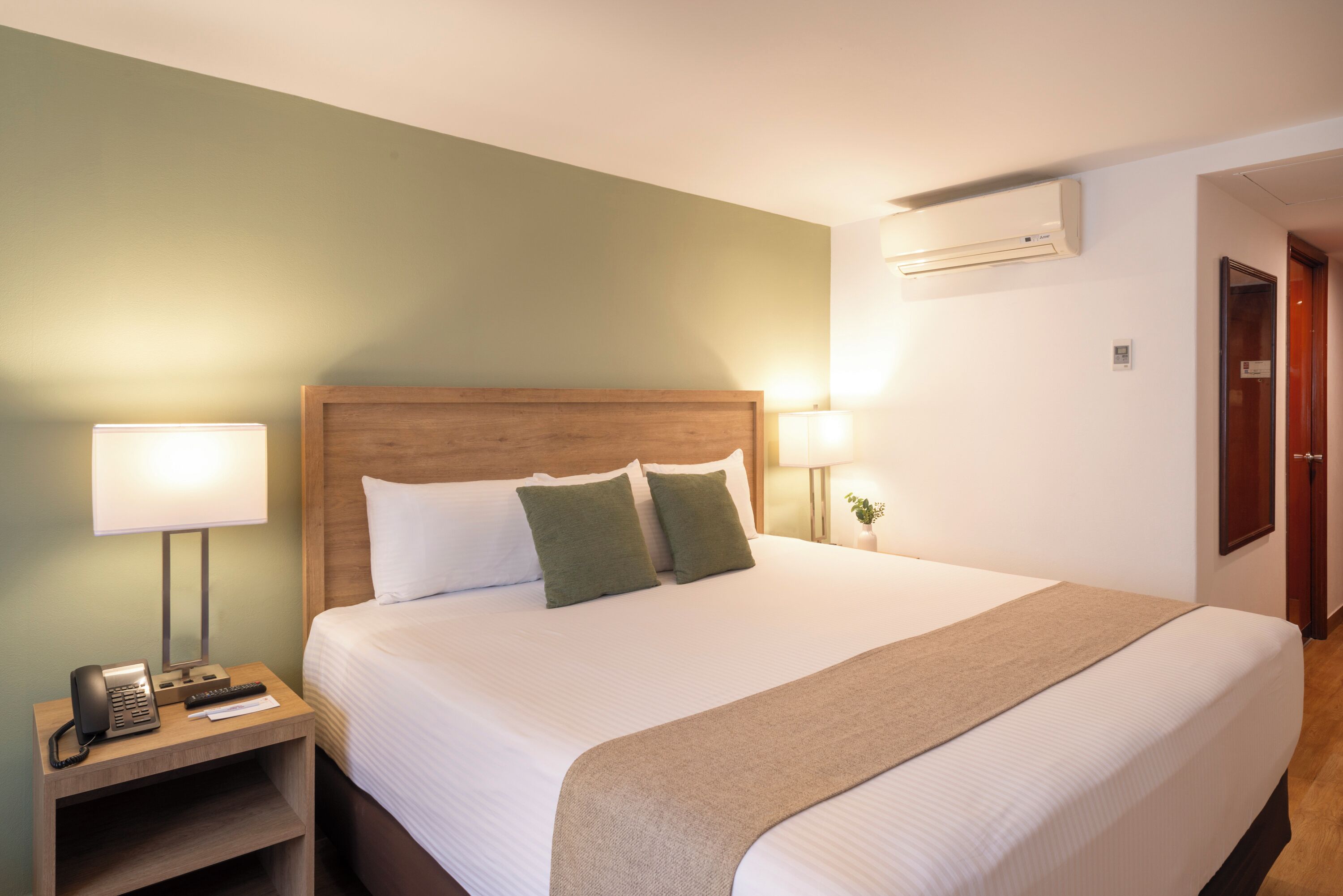 Habitación de hotel con cama, lámparas de noche, teléfono y aire acondicionado.