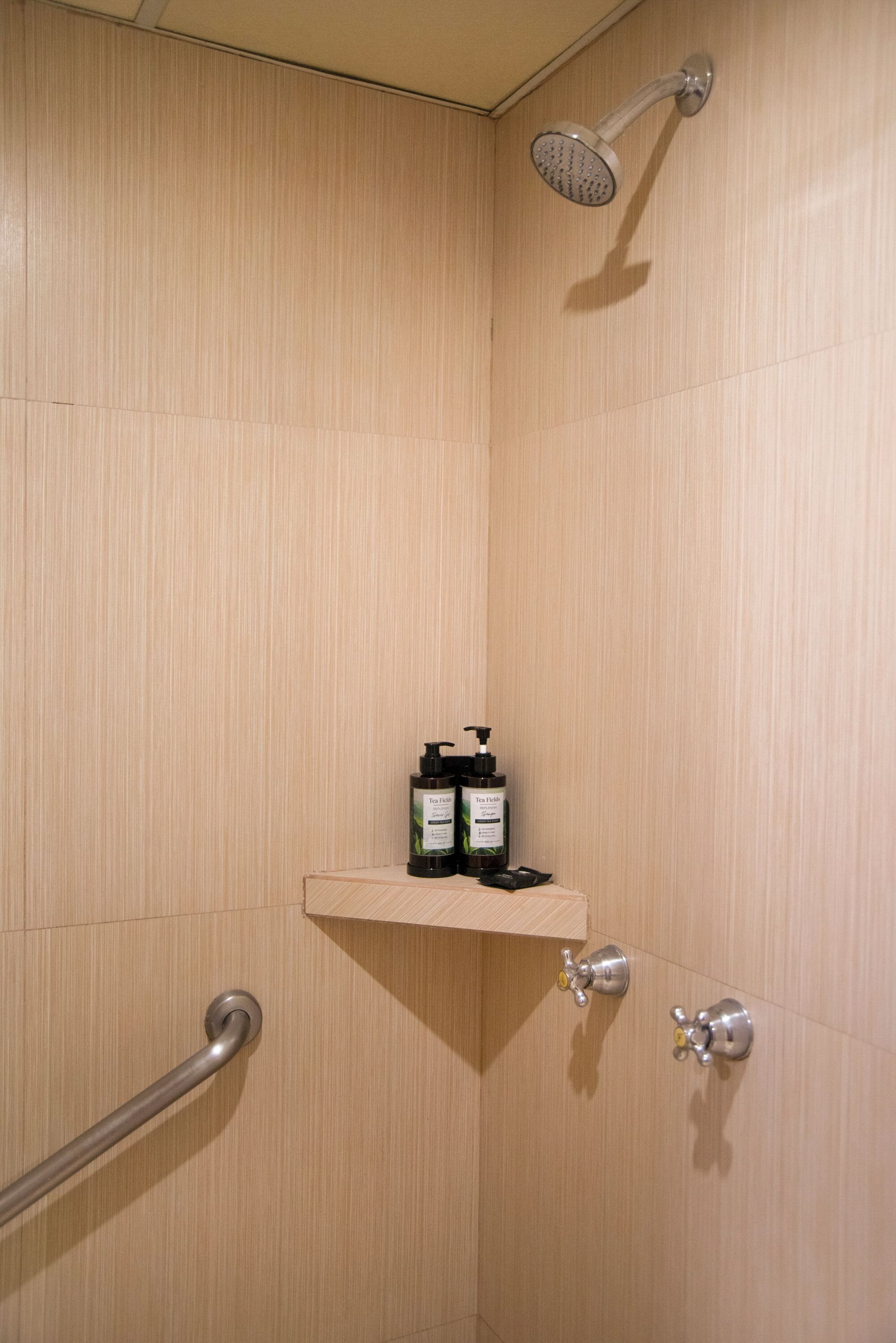 A shower area with a wooden wall, a shelf with toiletries, and a handrail.