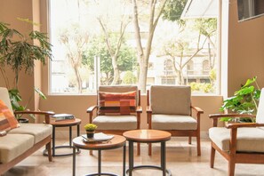 A cozy seating area with two sofas, a chair, and a small table, all arranged around a large window offering a view of trees and buildings. - Hotel Stanza (Mexico City)