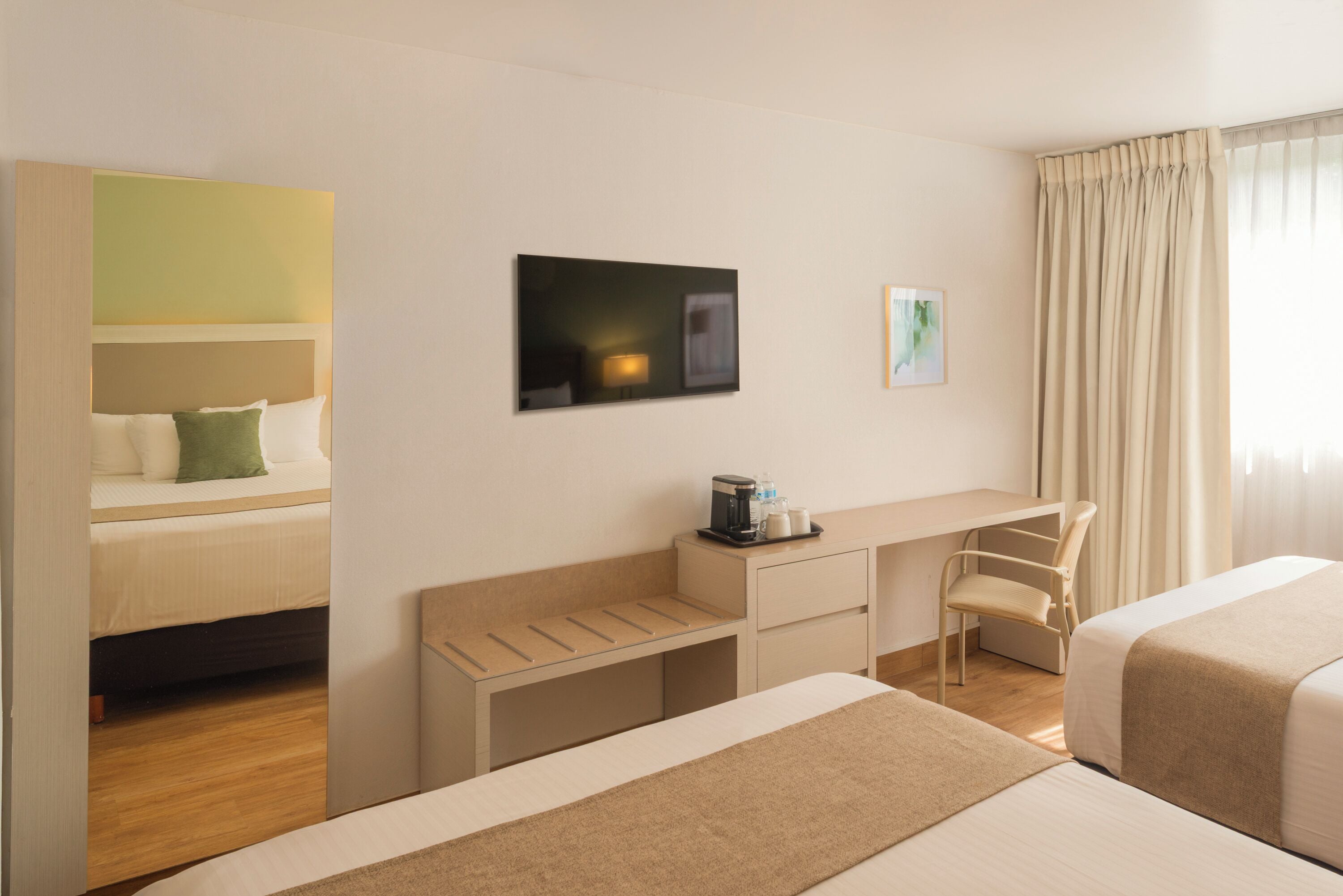 Habitación de hotel con dos camas, un escritorio, una silla, un televisor y una ventana con cortinas.