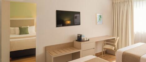 Habitación de hotel con dos camas, un escritorio, una silla, un televisor y una ventana con cortinas.