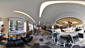 A modern hotel lobby with a curved bar, seating areas, and large windows offering city views. - Hotel Stanza (Mexico City)