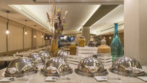 A restaurant with a modern interior, featuring a long dining area with tables and chairs, a decorative vase with dried plants, and a large blue vase on the counter. - Hotel Stanza (Mexico City)
