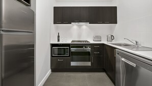 A modern kitchen with stainless steel appliances, dark cabinetry, and a white countertop. - Quest Dandenong (Dandenong)