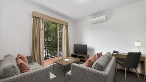 A modern living room with a sofa, armchair, coffee table, TV, and desk with a chair. - Quest Dandenong (Dandenong)