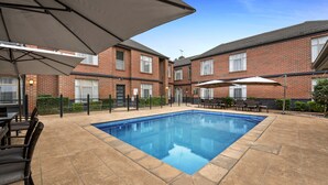 A rectangular swimming pool with a tiled deck, surrounded by brick buildings with windows and doors. - Quest Dandenong (Dandenong)