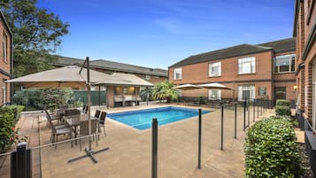 A residential backyard with a swimming pool, patio furniture, and a brick house.