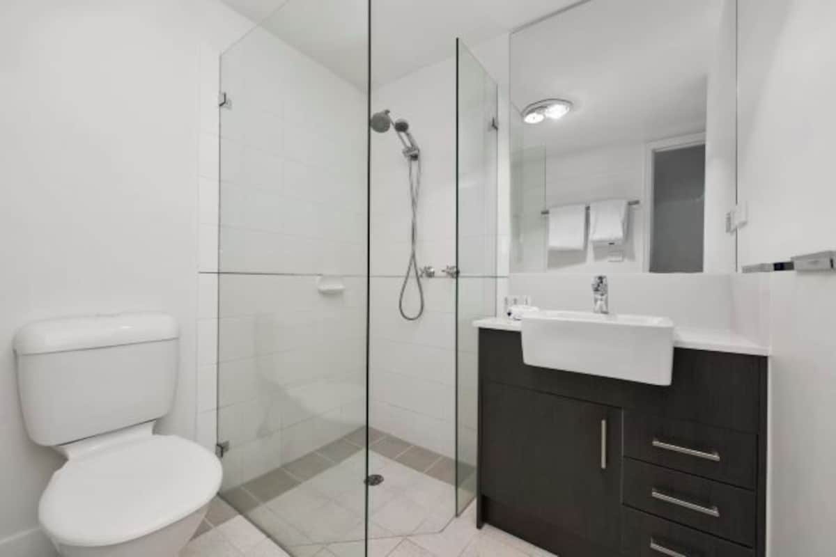 A modern bathroom with a glass-enclosed shower, a white toilet, and a dark wooden vanity with a white sink.