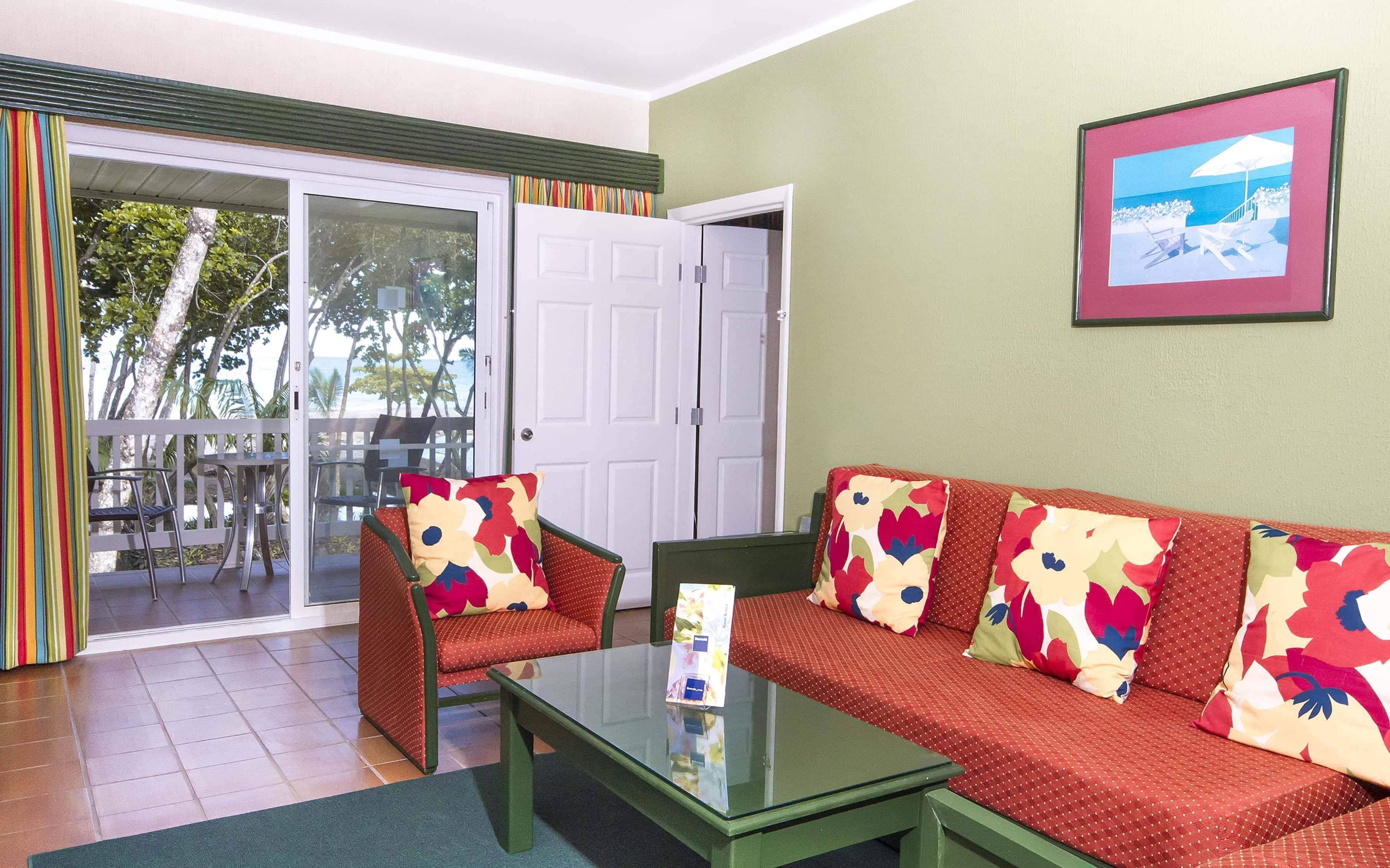 Una habitación con sofá, sillones, una mesa de centro de vidrio y una puerta que da a un espacio exterior con vista al océano.