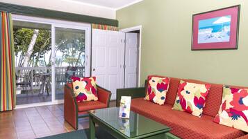 Una habitación con sofá, sillones, una mesa de centro de vidrio y una puerta que da a un espacio exterior con vista al océano.