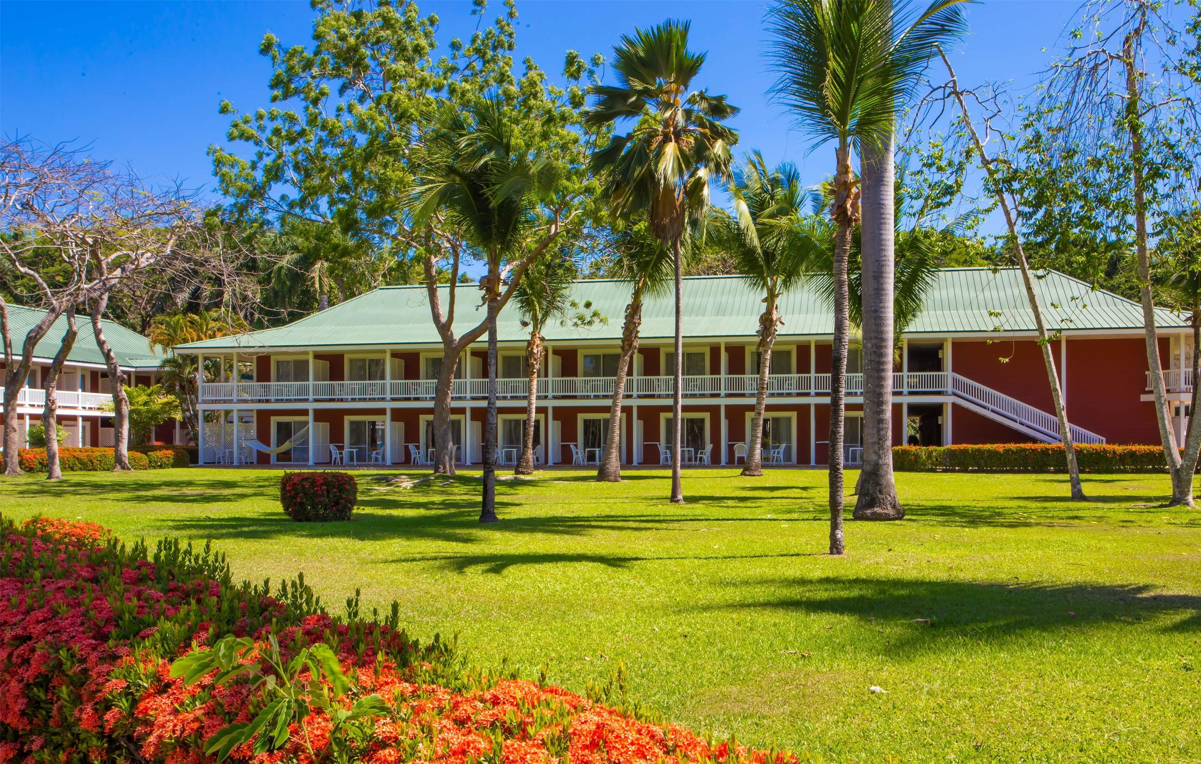 Ein Hotel mit begrüntem Dach, weißen Balkonen und einem gepflegten Rasen mit Palmen und roten Blumen.