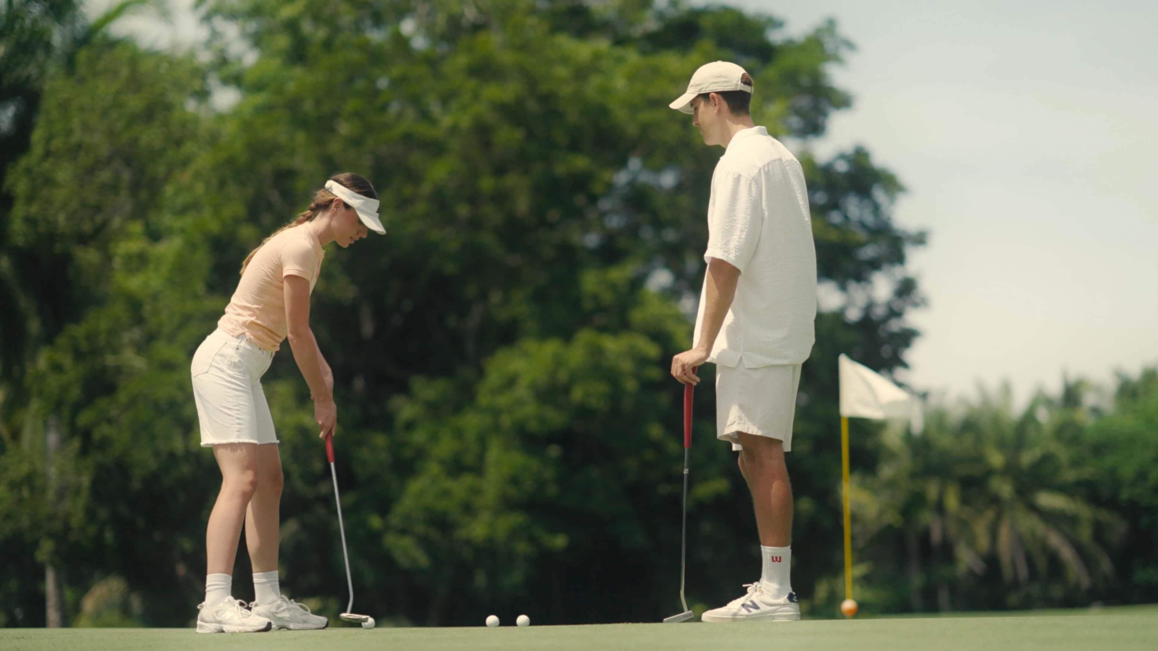 Dos personas en un campo de golf, una a punto de hacer un putt y la otra observando.