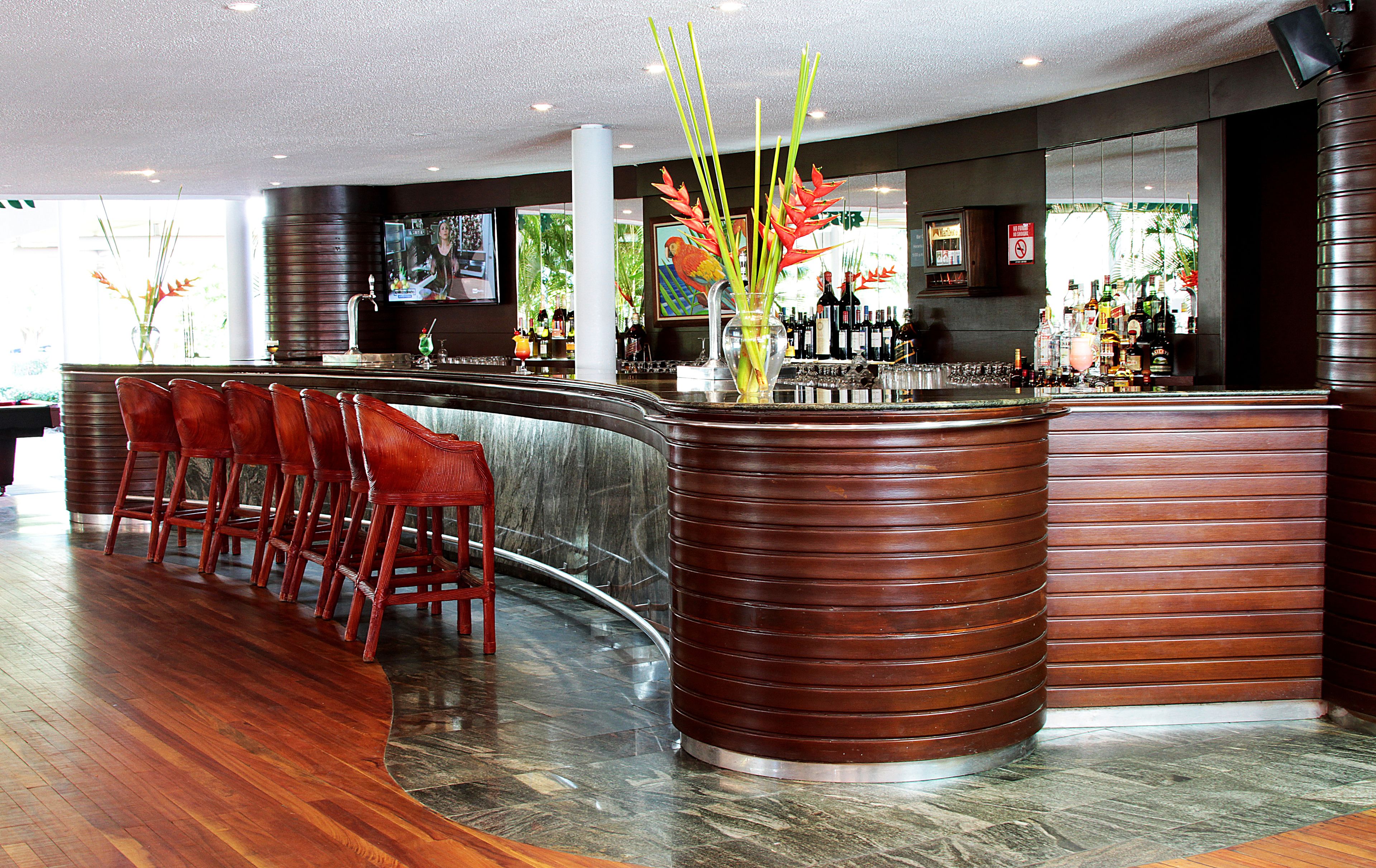 Una zona de bar con sillas de madera, un mostrador curvo y un jarrón grande con flores.