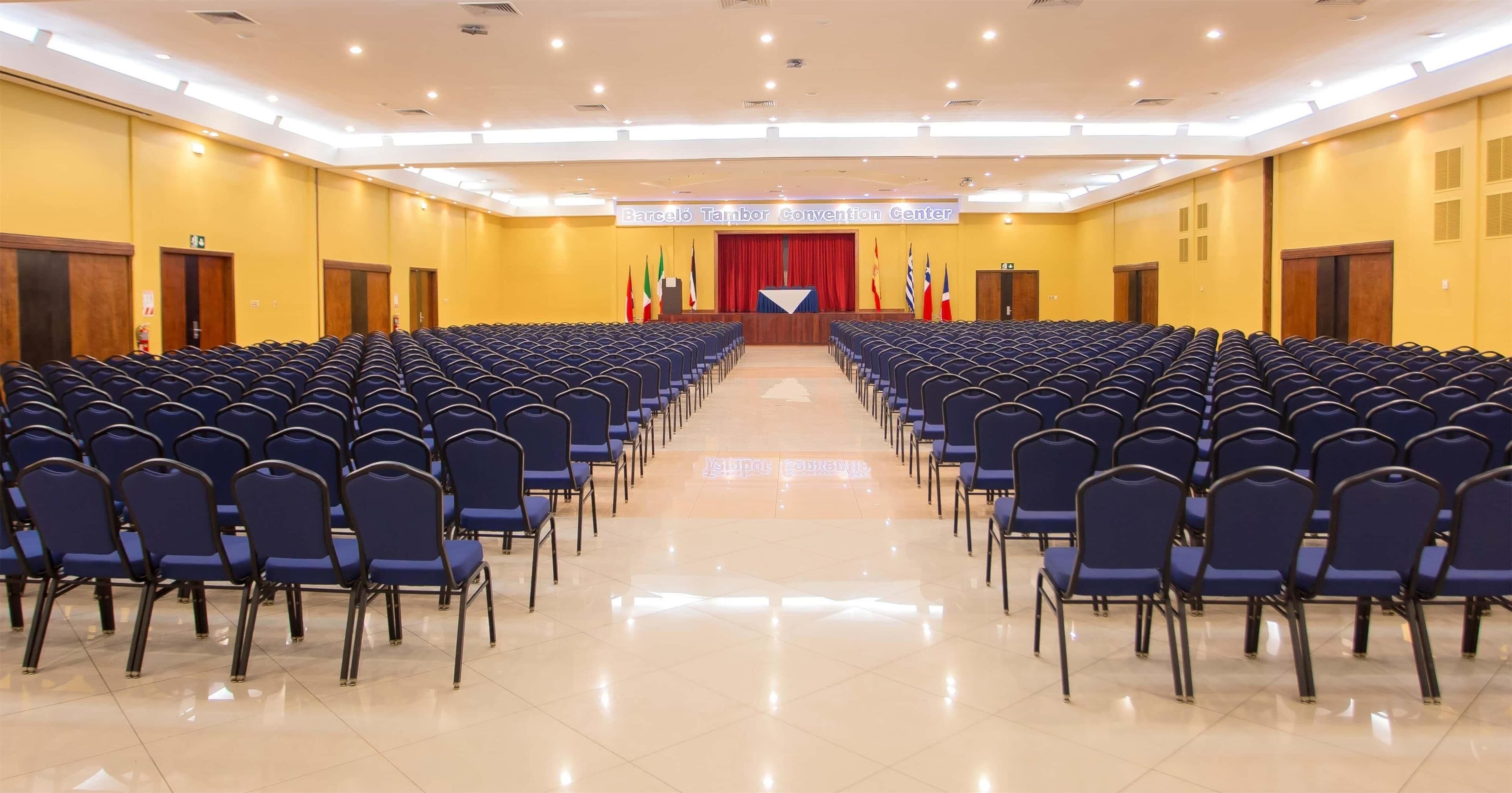 A conference room with rows of chairs facing a stage, flags, and a podium.