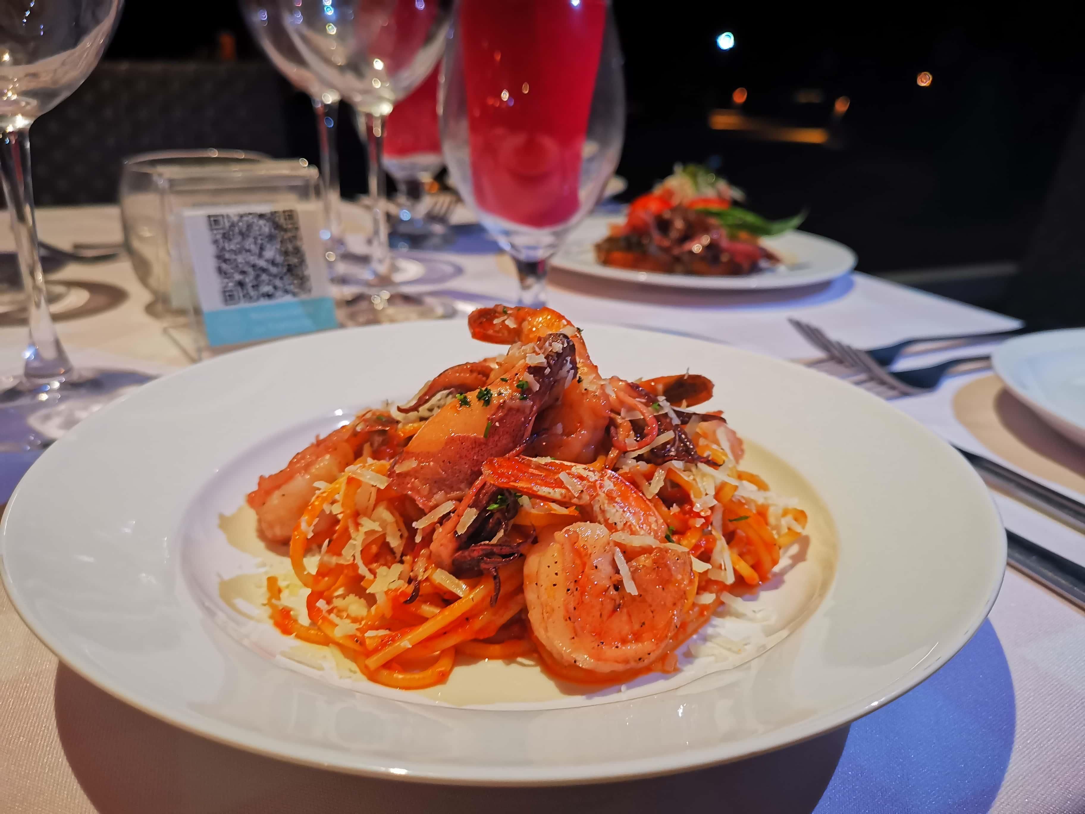 Una mesa de comedor con platos de comida, copas de vino y un código QR en una servilleta.