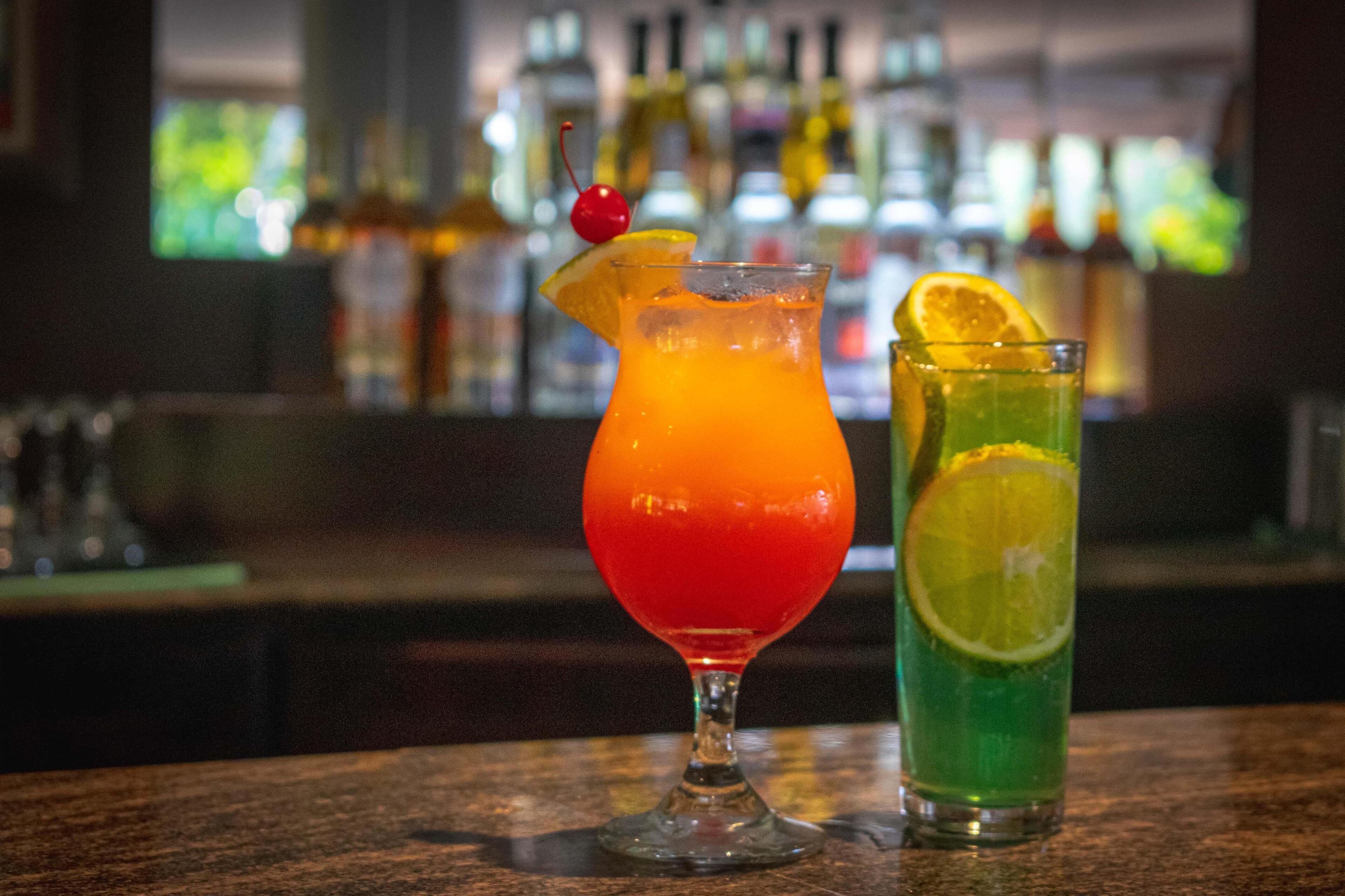 Deux cocktails sur le comptoir d’un bar, avec un arri ère-plan flou composé de bouteilles.
