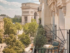 A balcony with a view of the Arc de Triomphe, trees, and a dining area with chairs and a table. - Hotel Cecilia (Paris)