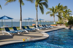 A poolside area with lounge chairs and umbrellas, a clear view of the sea, and a tiled pool.