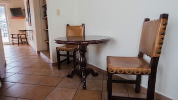 A dining area with a round table and two wooden chairs, a tiled floor, and a white wall.