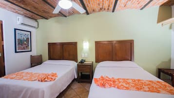 Een kamer met twee bedden, een plafondventilator, een airconditioning en een klein nachtkastje met een lamp.