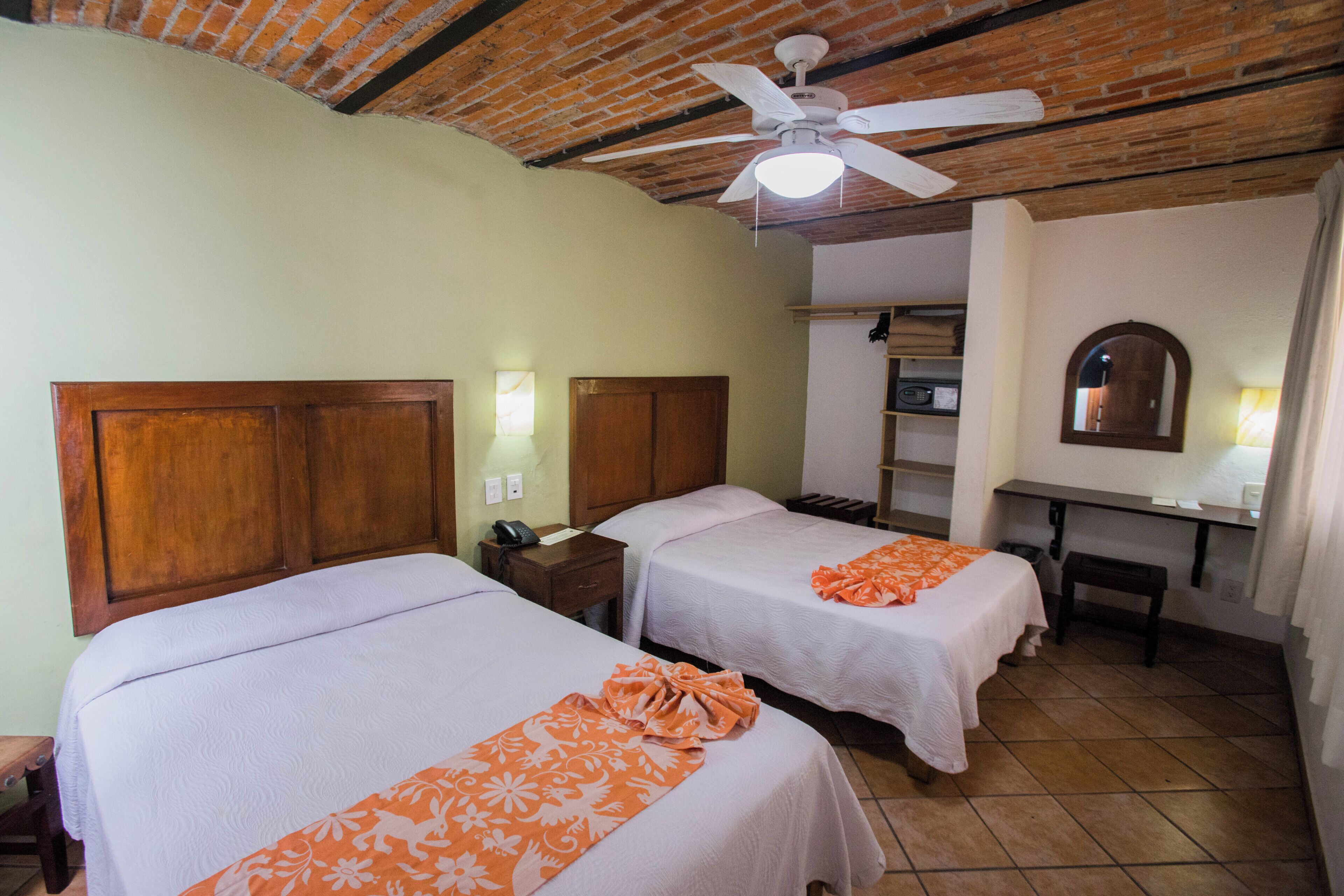 A room with two beds, a desk, a ceiling fan, and a mirror.