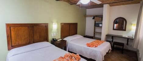 A room with two beds, a desk, a ceiling fan, and a mirror.
